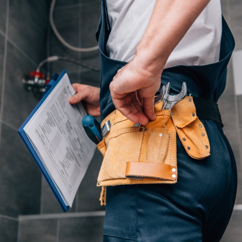 cropped shot of male plumber with clipboard and toolbelt standing in bathroom