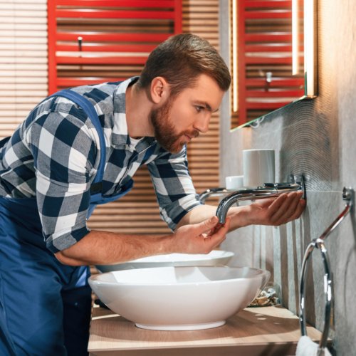 Plumber in blue uniform is at work in the bathroom.