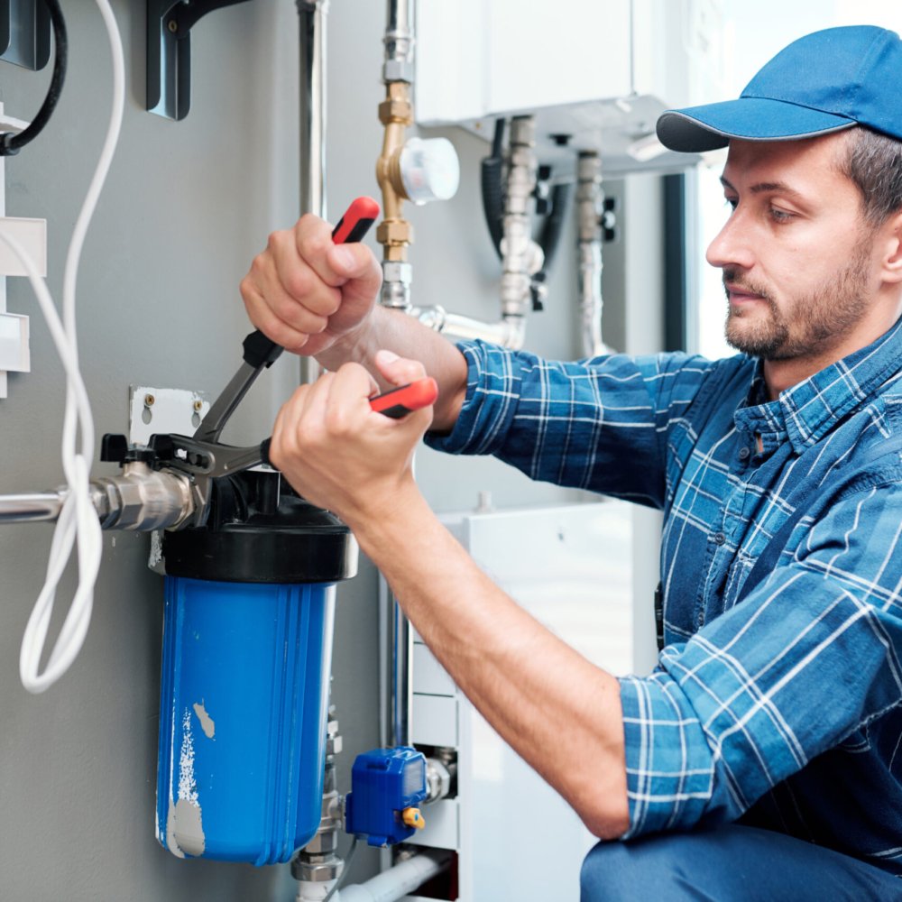 Young plumber or technician in workwear using pliers while installing or repairing system of water filtration